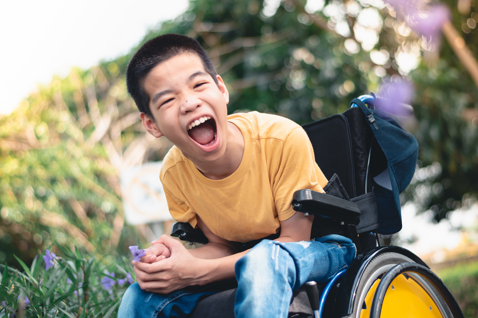 A young boy laughs after picking a flower outside, he is using a wheelchair