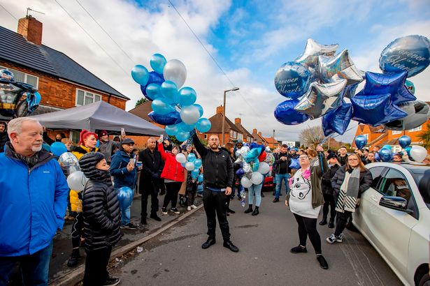 Group of people on street all holding blue balloons