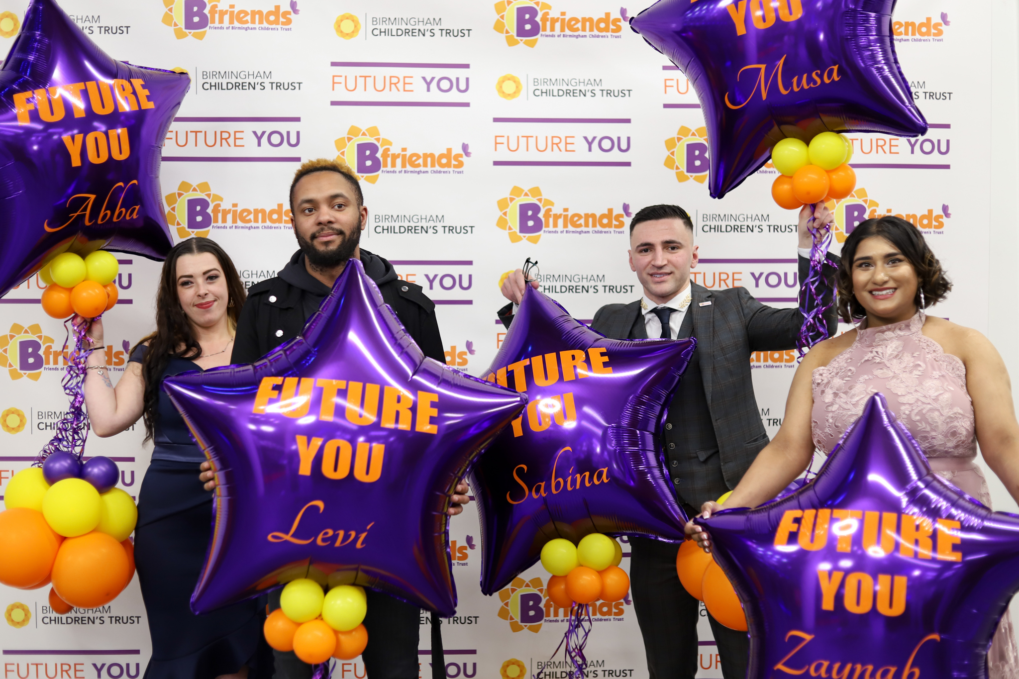 Four young people posing with purple and orange balloons