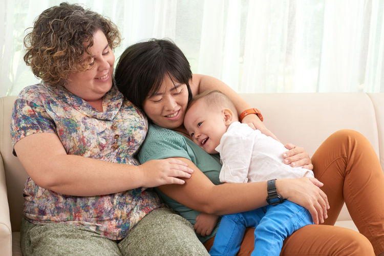 A lesbian couple cuddle their young son on the sofa