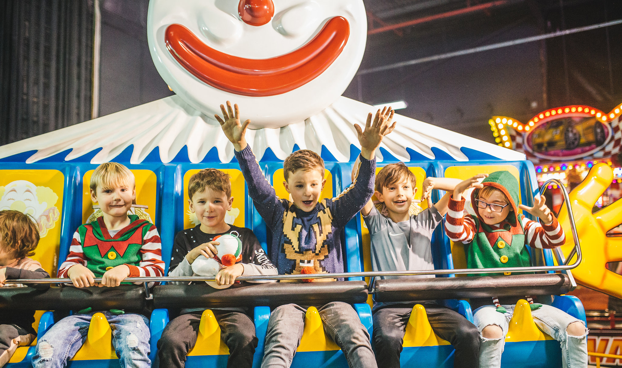 Five children on a fair ground ride with arms in the air and smiling