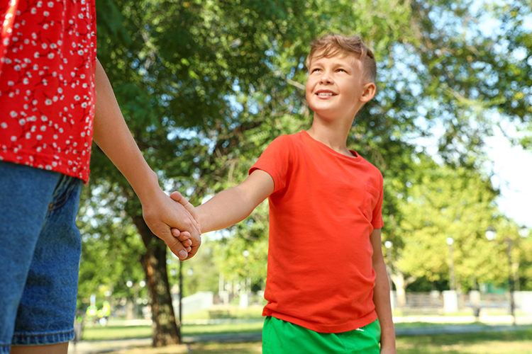 A young boy looks up at his foster carer. They are holding hands and walking in the park