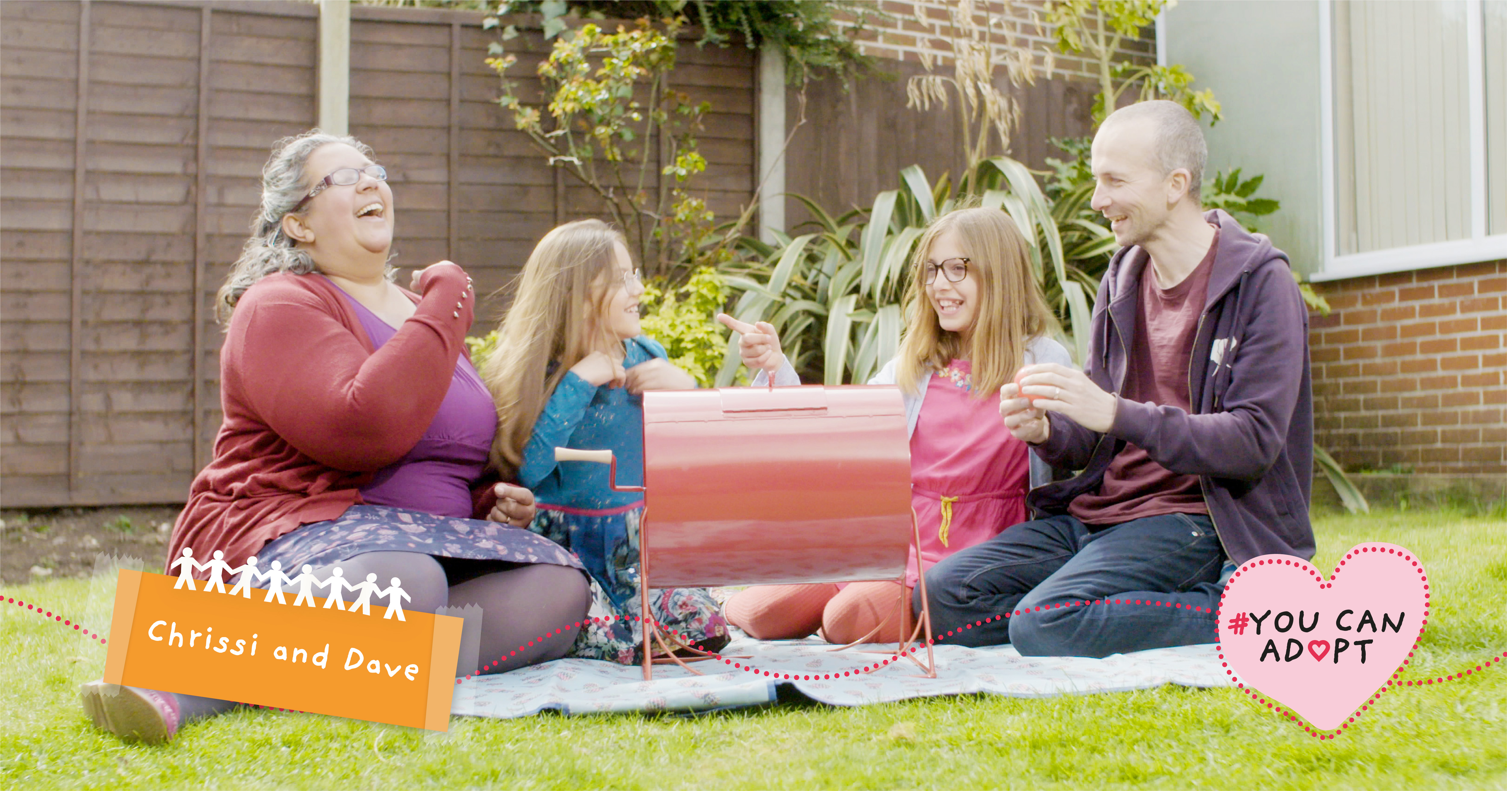 A mum, dad and their two daughters sit on a picnic blanket in their garden.